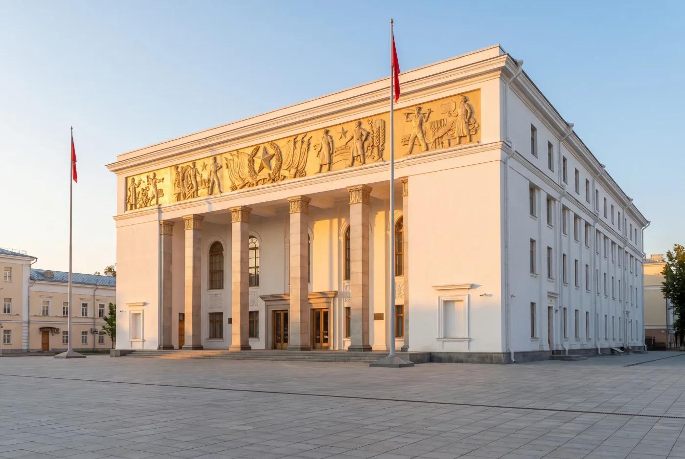 Классическая реставрация Дом культуры после классической реставрации — белая штукатурка, выделенные колонны, золотые барельефы, флагштоки у входа, AI-рендер